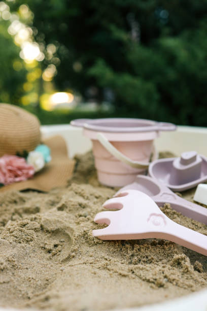 istock Plastic sandbox toys, including a bucket, sieve, rake, and boat, arranged in a backyard sandbox. Soft pastel colors contrast with natural greenery, creating a playful and serene outdoor setting 2201643049
