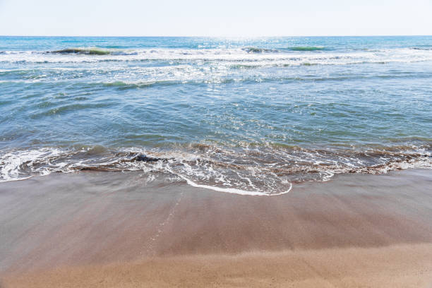 Low angle view of golden sand and sea on a sunny summer day. Yellow and blue, sand and sea surface texture.