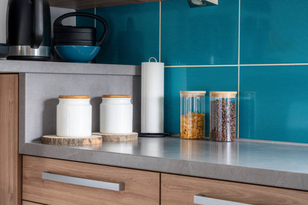 Modern kitchen counter with glass and ceramic jars containing coffee and cereals, against a blue tiled wall