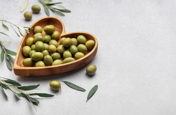 istock Fresh green olives displayed on wooden heart shaped bowl with olive branches 2201649306