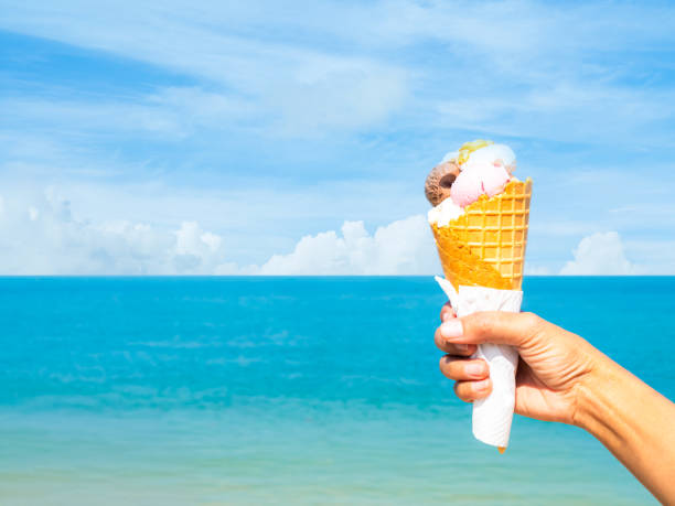 istock Summer background, hand holding ice cream cone on blue sea and cloud sky in summer tropical season holidays at island, woman travel vacation holidays in nature ocean. 2201655838
