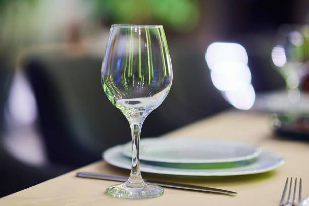 istock A wine glass sits on a table with a white plate and silverware. The table setting is elegant and sophisticated, with a focus on the wine glass as the centerpiece. 2201656386