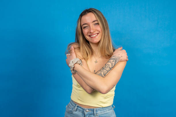 istock Smiling young woman hugging herself on blue background 2201657085
