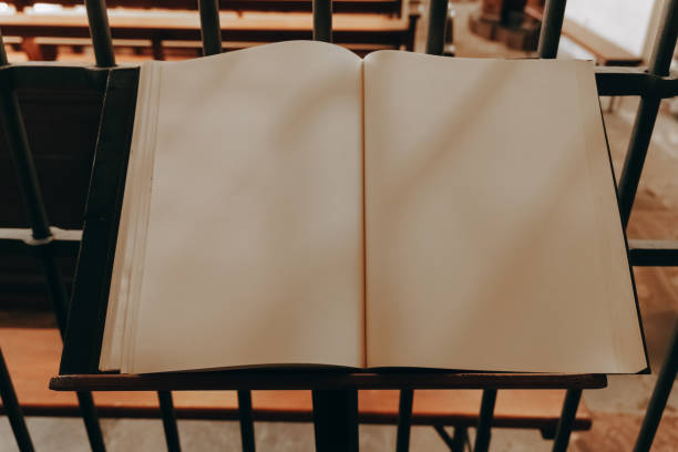 Open blank book on a stand in a library surrounded by wooden shelves and iron railings in the late afternoon light stock photo