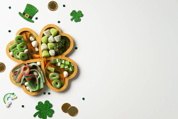 istock Patrick's Day candy assortment in a four-leaf clover-shaped tray, surrounded by festive decorations like glittery shamrocks, gold coins, and a leprechaun hat on a white background. 2201660935