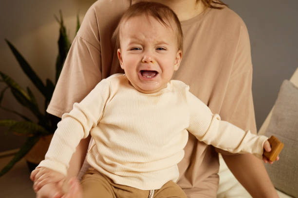 istock A baby bursts into tears while being held by a mother in a warm, inviting indoor space filled with plants. The mother comforts the child but seems unsure how to soothe the distress 2201662235