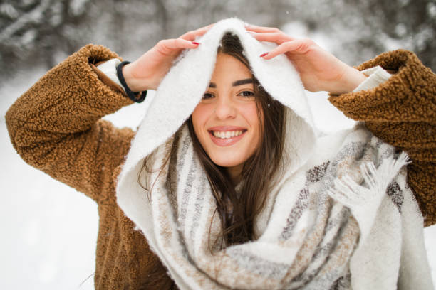 Close-up portrait of happy young woman with big scarf over her head looking at camera in snowy nature