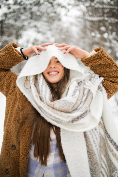 Portrait of happy young woman with big scarf over her head looking at camera in snowy forest