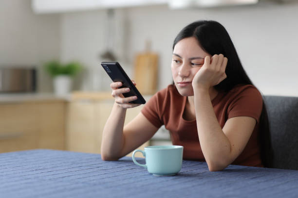Bored asian woman checking phone in the kitchen stock photo