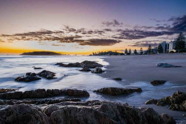 istock Serene beach sunrise with rocky foreground. 2201672559