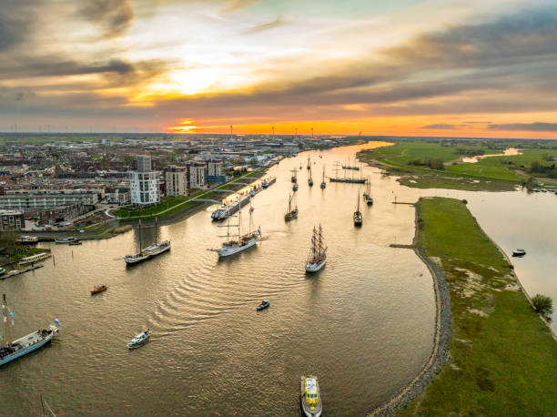 Kampen and river IJssel during the traditional fleet review or naval review at the start of the 2024 Sail Kampen event in the Hanseatic League city at the end of a springtime day with a colorful sunset in the sky.