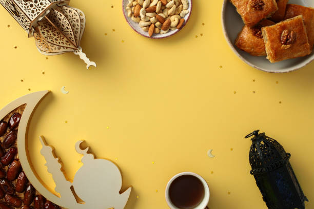 Ramadan flat lay with traditional lanterns, dates, nuts, baklava, and cup of tea on a yellow background with star and crescent moon decorations. Perfect for celebrating and Ramadan and Eid themes