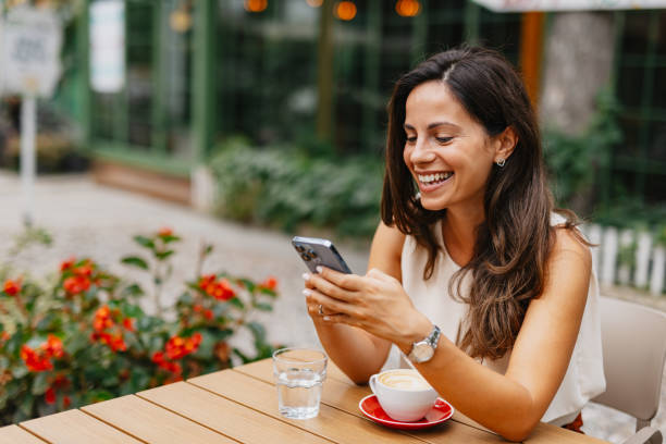 istock Young business woman laughing while using mobile phone at outdoor cafe 2201680361