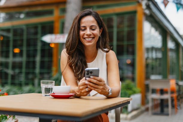 istock Smiling businesswoman using smartphone and drinking coffee at outdoor cafe 2201680382