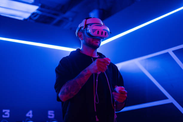 istock Professional man gamer with VR glasses holding joysticks and playing virtual game with neon light. Technology and augmented reality 2201682662