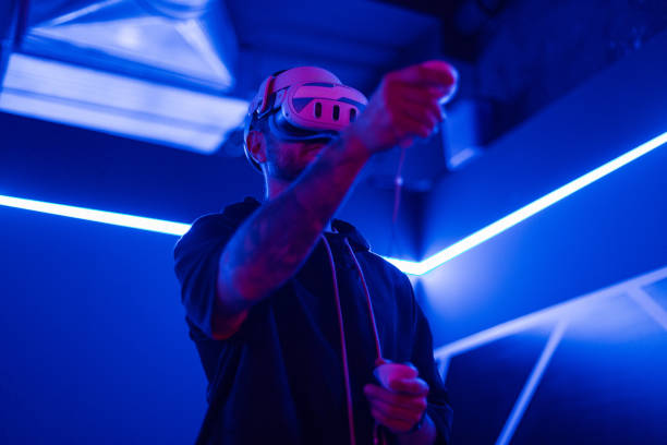 istock Cool man with VR glasses plays games with joysticks in neon light. Metaverse, virtual reality glasses and a man with vr control futuristic gaming, cyber and 3d world. Gamer person 2201682702