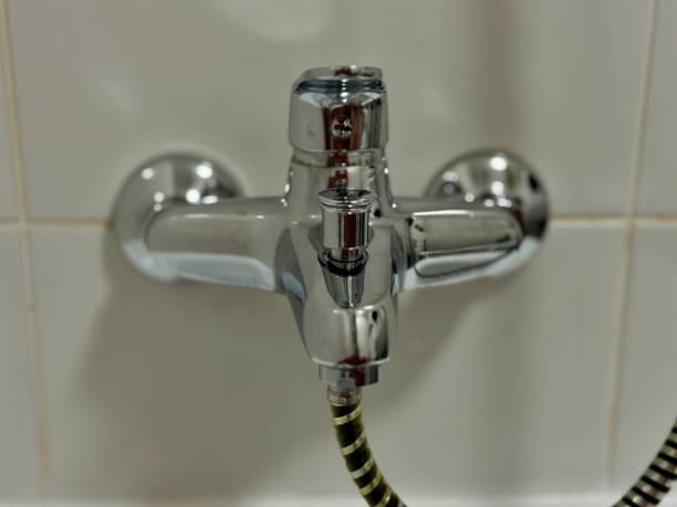 Chrome water faucet in bathroom against white tile backdrop. High quality photo