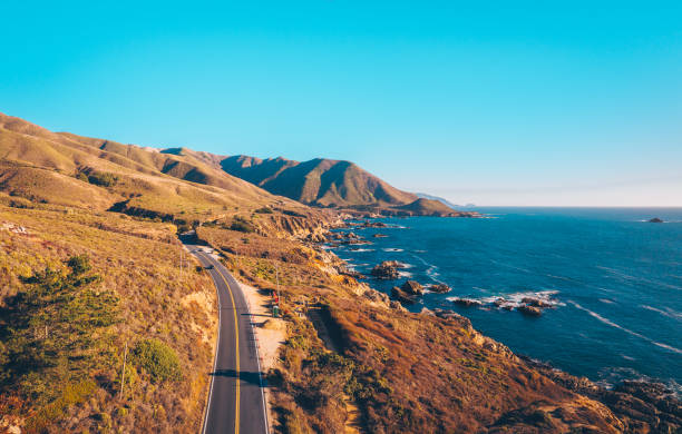 Breathtaking coastal views along the Pacific Coast Highway in California, where a winding road follows the dramatic cliffs and blue ocean. This iconic scenic drive captures the beauty of the West Coast’s rugged shoreline.