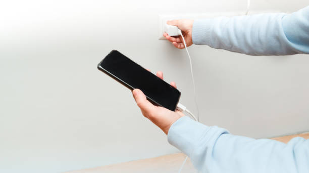 istock Female holding phone while charging from wall outlet. Woman using charging power to smart phone. 2201687421