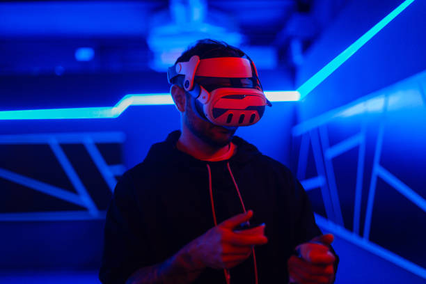 istock Handsome stylish cool gamer man with VR glasses holding joysticks and playing virtual game in neon light gaming room. Virtual reality technology 2201688445