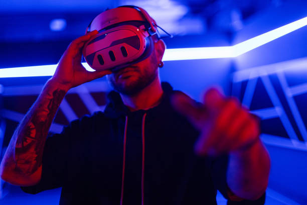 istock Cool handsome fashion tech man with VR glasses control virtual menu and touch finger in dark room with neon light 2201688846