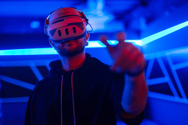 istock Cool tech man with VR headset glasses controls virtual menu and touches with finger in dark room with neon light 2201688848