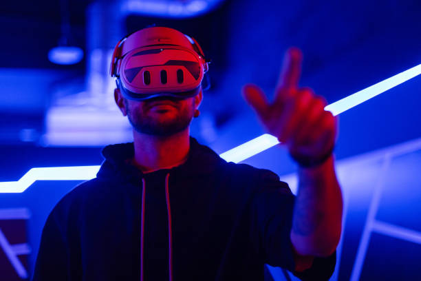 istock Cool tech man with VR headset glasses controls virtual menu and touches with finger in dark room with neon light 2201688887