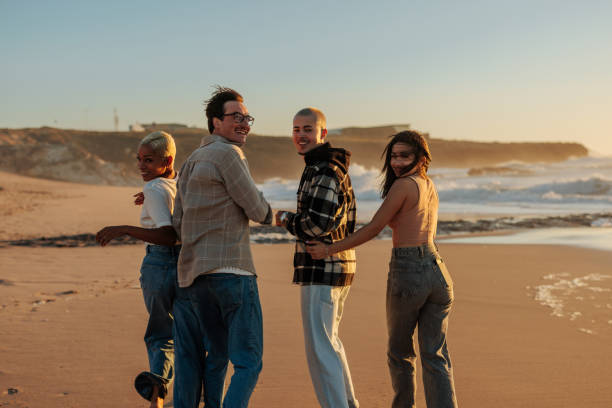 istock Friends walking on the beach at sunset holding hands 2201688937