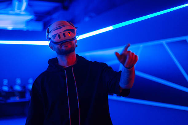 istock Cool tech man with VR headset glasses controls virtual menu and touches with finger in dark room with neon light 2201689067