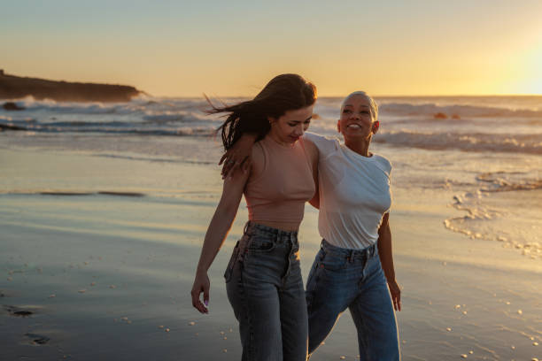 istock Two friends walking on beach at sunset, embracing diversity and friendship 2201689120