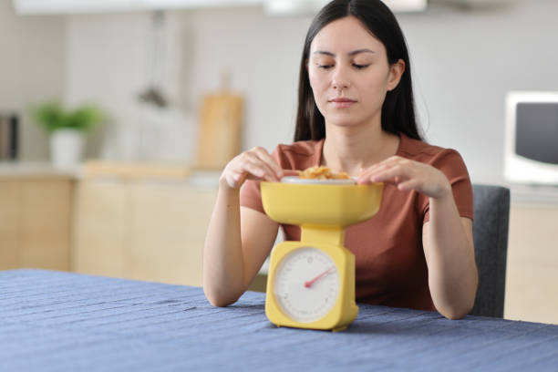 istock Serious asian woman weighing food using scale in a kitchen 2201691062