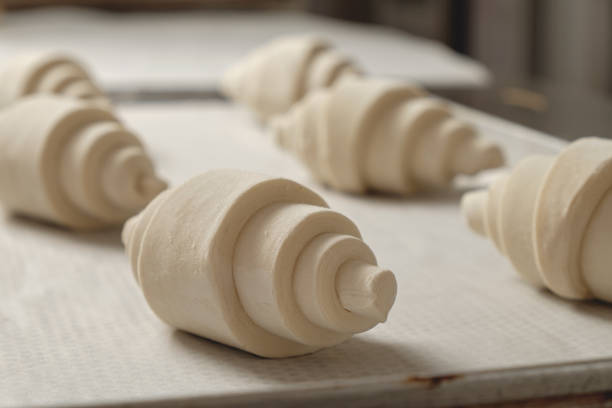 Freshly formed croissants resting on a parchment-lined tray in a warm bakery, ready for the oven to transform them into a flaky breakfast delight
