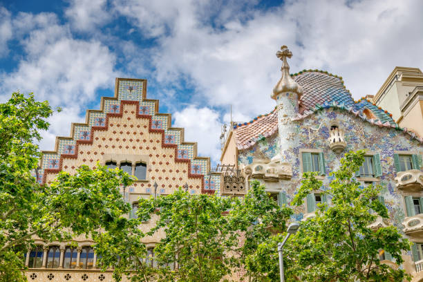 istock Two distinct and architecturally unique buildings, partially obscured by green trees, under a blue sky with scattered clouds in Barcelona 2201692155