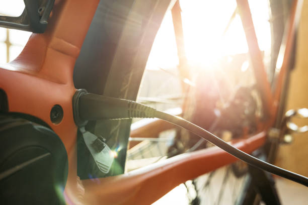 Detail view of an orange electric bicycle charging outdoors, emphasized by the back wheel and strong sunlight glare