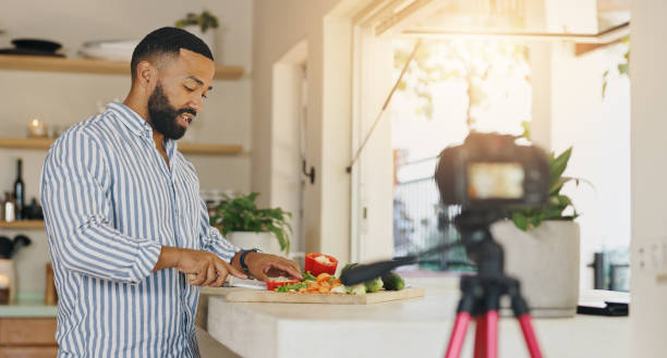 istock Camera, live streaming and man in kitchen for cooking tutorial, cuisine and meal preparation in home. Culinary influencer, content creator and person with food, recipe or ingredients for social media 2201699755