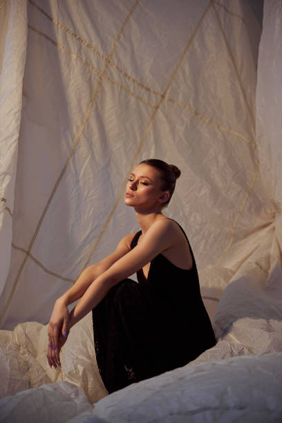 Woman dressed in a sleek black outfit sits gracefully against a soft, draped backdrop
