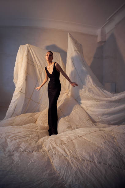 model stands gracefully on a sprawling fabric backdrop, showcasing a sleek black dress. studio atmosphere is creative, enhanced by soft lighting and unique textures
