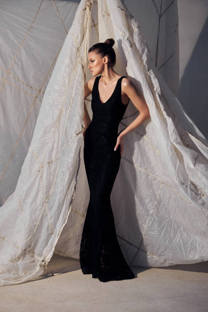 istock model stands gracefully in a fitted black dress with a flared bottom, showcasing a minimalist style. backdrop features soft, draped fabric, enhancing the overall aesthetic of the setting 2201700667