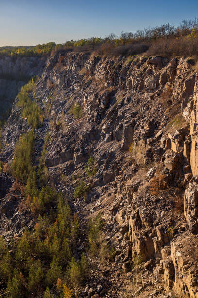 istock Rocky cliff with rough textures, golden sunlight, and sparse vegetation. The rugged terrain highlights natural erosion, with scattered dry plants and earthy tones dominating the landscape. 2201700747