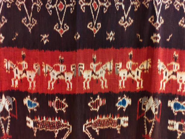 A traditional woven fabric featuring intricate patterns of human figures on horseback, animals, and geometric motifs A traditional woven fabric featuring intricate patterns of human figures on horseback, animals, and geometric motifs. The textile appears to be an ikat from Flores Island, Indonesia ikat textiles at indonesian textile market stock pictures, royalty-free photos & images
