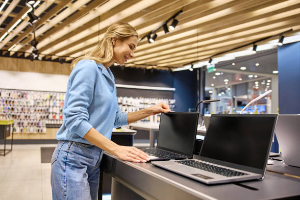 istock A cheerful woman smiling as she carefully evaluates various laptops in a modern electronics store 2201703945