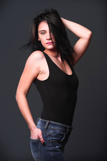 istock Model poses confidently in black tank top and jeans against dark backdrop 2201709557