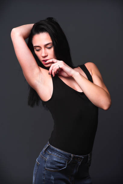 istock Model poses gracefully in a black tank top and jeans against a dark backdrop 2201709791