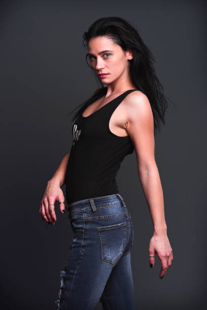 Model poses confidently in fitted jeans and a black top against a dark backdrop
