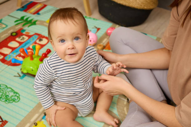 istock A toddler sits on a vibrant play mat, smiling while exploring toys. A caregiver gently interacts with the child in a cozy indoor setting, promoting playtime joy 2201711546