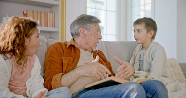 istock Grandfather Reading to Curious Grandchildren on Sofa 2201712667