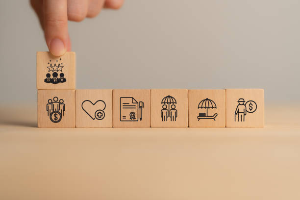 istock Employee benefits concept. A hand stacking wooden blocks with icons representing various employee benefits, including financial security, health insurance, retirement planning, and vacation time. 2201713650