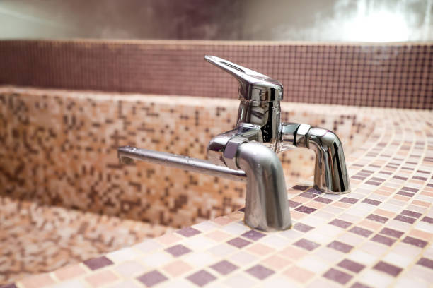 A close-up of a shiny vintage-style bathtub faucet with white accents against a sea green tiled background, typical of a classic boutique hotel's attention to period details.