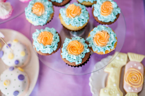 Birthday party concept. Table for kids with cupcakes with blue and orange top and decor items in bright pink and blue colors
