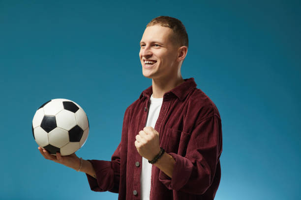istock Smiling Man Holding Soccer Ball Against Blue Background 2201722054